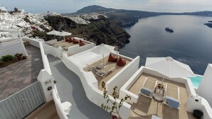 Une terrasse sur le toit, avec des murs blancs, des chaises longues et des parasols, offrant une vue sur une ville côtière et la mer.