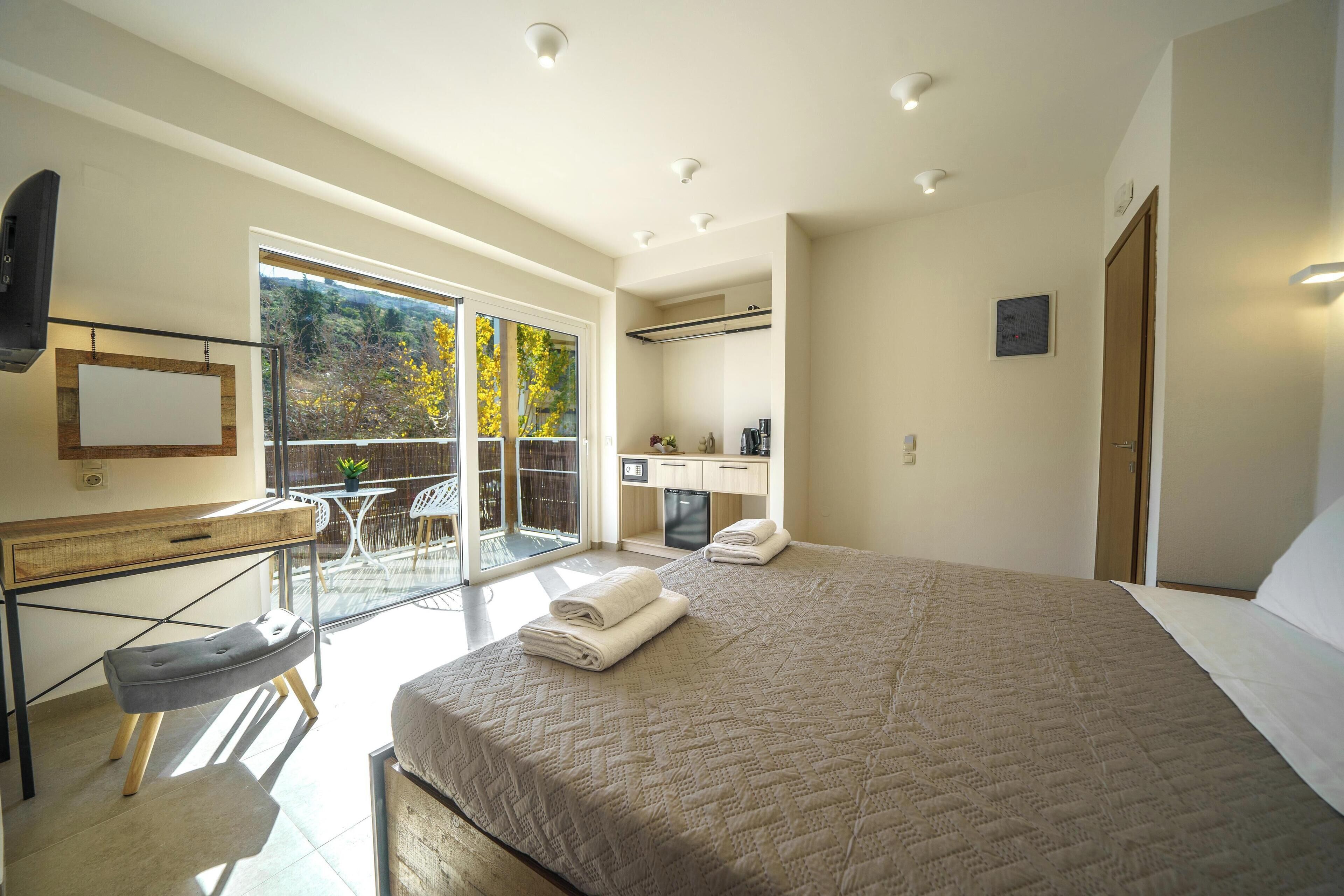A modern bedroom with a large bed, a desk, and a view of a balcony.