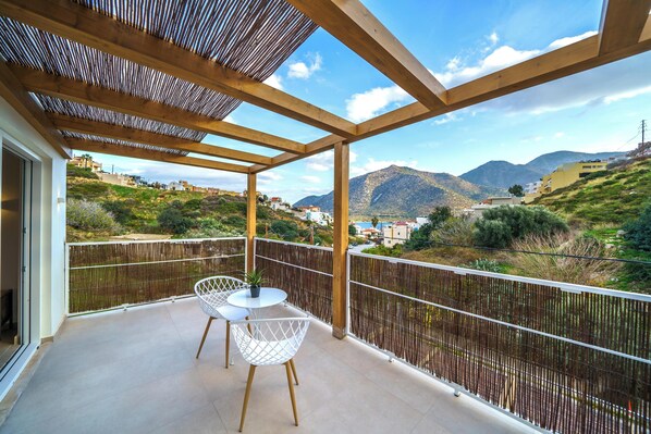 A balcony with a view of a mountainous landscape, wooden pergola, and white wire chairs. - My Bali Suites (Mylopotamos)