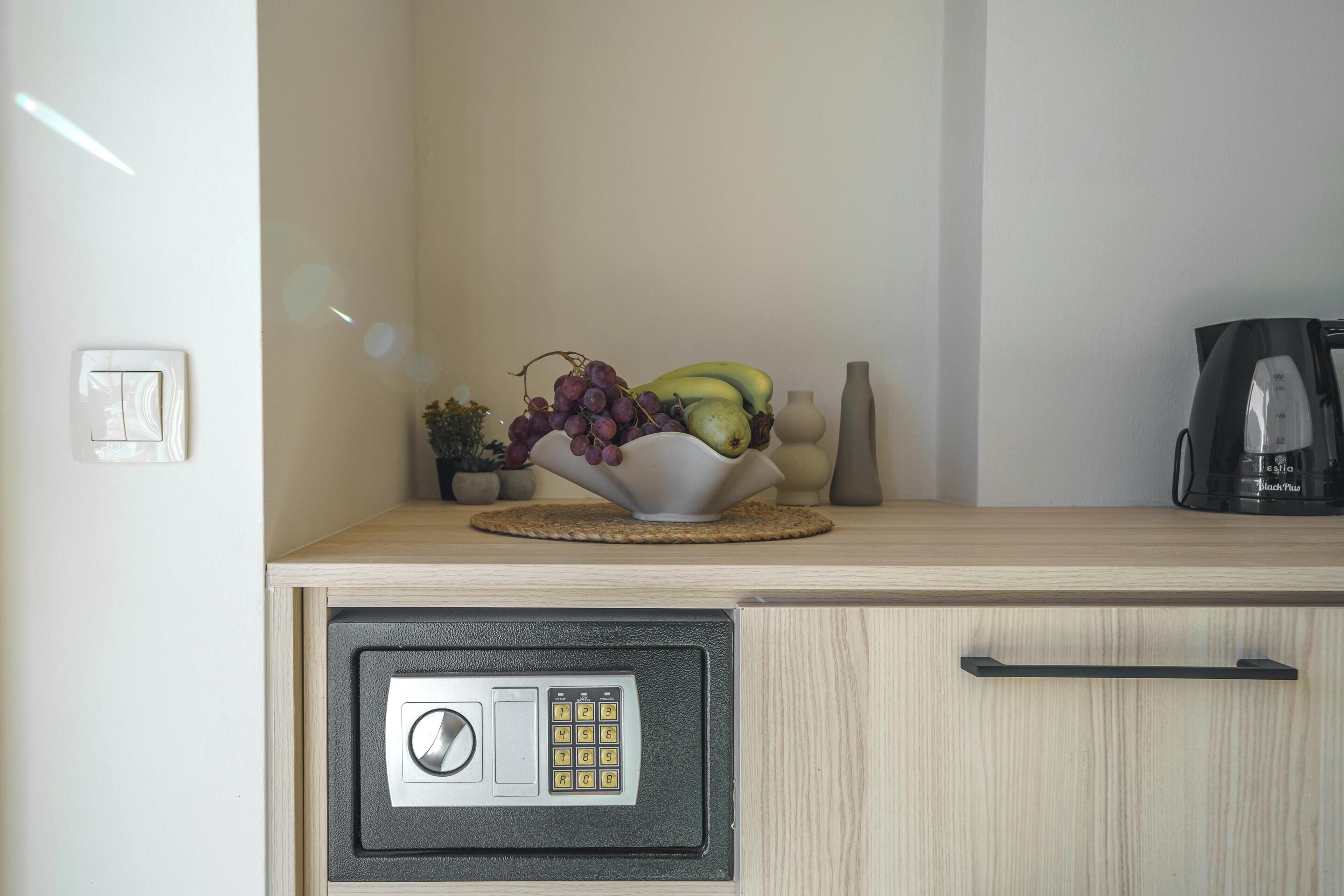 A kitchen counter with a fruit bowl containing grapes, bananas, and a pear. There is a coffee maker and a vase on the counter.
