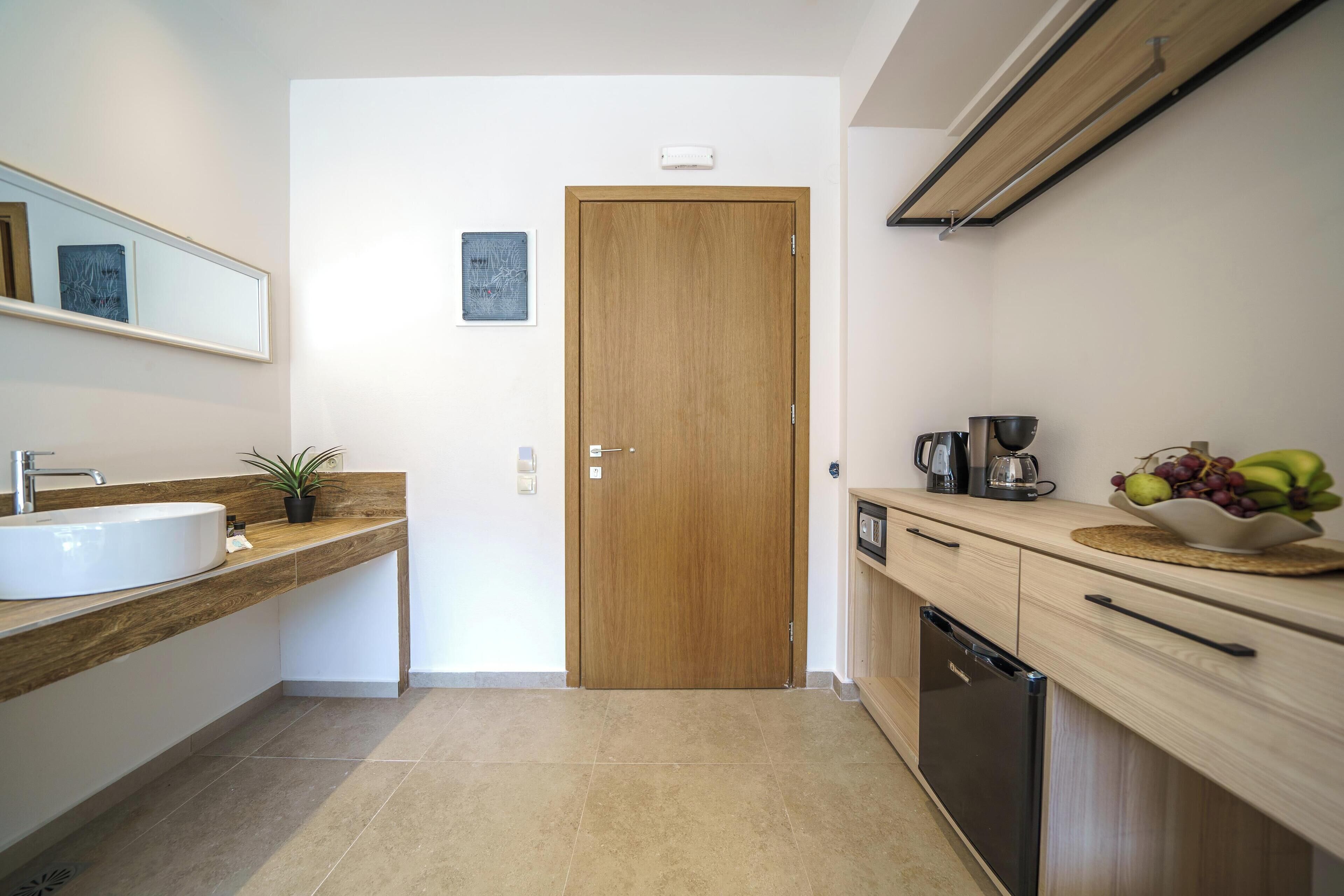 A modern kitchen with a wooden door, a sink, a countertop with a plant, and a coffee maker.