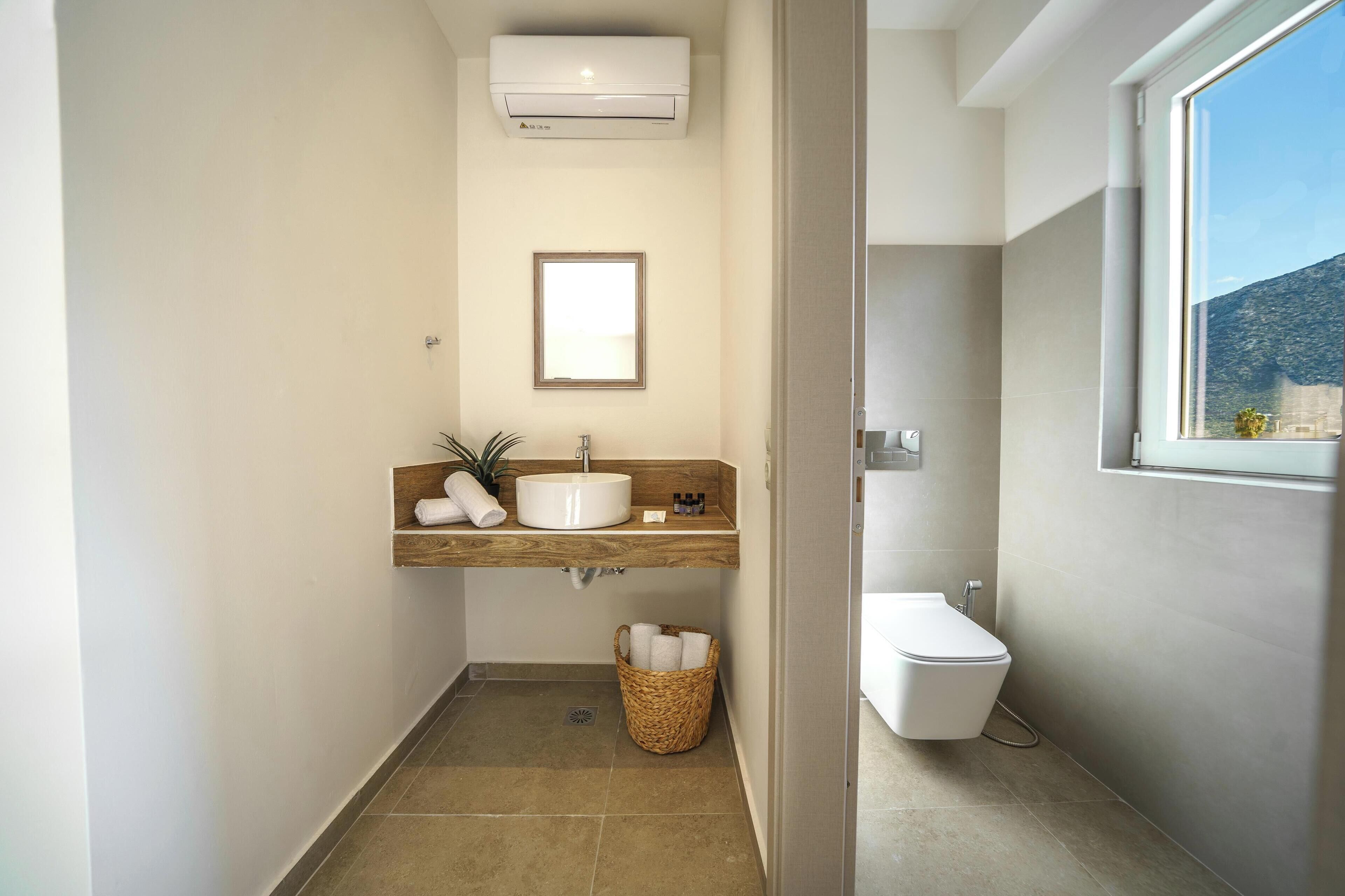 Un baño moderno con tocador de madera, un lavabo blanco, un inodoro blanco y una ventana que ofrece vistas al exterior.