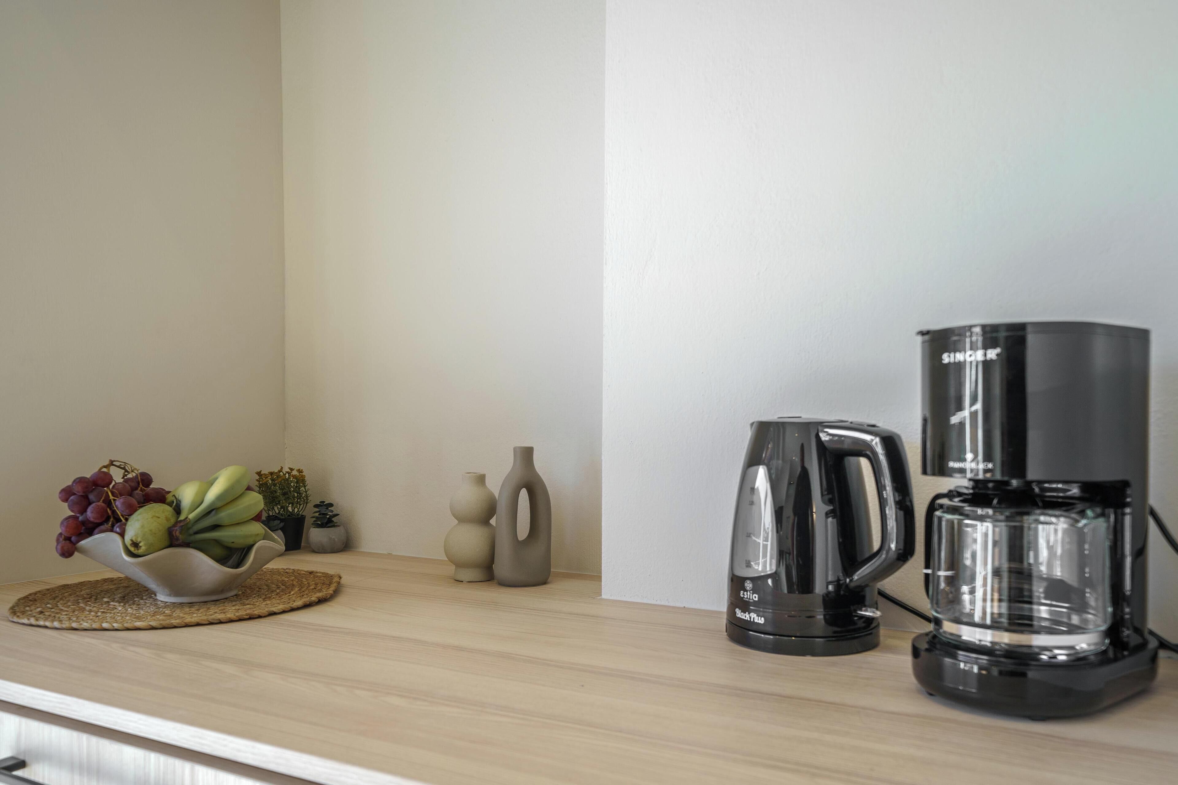 A kitchen counter with a coffee maker, a kettle, and a bowl of fruit.