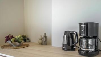 A kitchen counter with a coffee maker, a kettle, and a bowl of fruit.