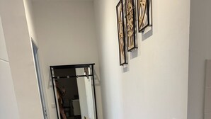 A hallway with a wooden floor, a small table with decorative items, and a mirror on the wall.