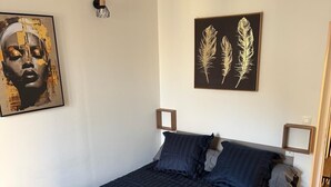 A bedroom with a bed, a nightstand, a wall-mounted lamp, and two framed artworks.