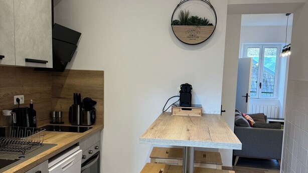 A modern kitchen with a wooden table and stools, a built-in oven, and a coffee machine.