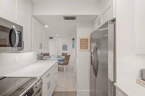 Eine moderne Küche mit einem Edelstahl-Kühlschrank, einem Einbauofen und einer Mikrowelle. Im Hintergrund ist ein Essbereich mit Tisch und Stühlen zu sehen.