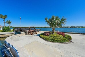A waterfront promenade with a wooden bridge, palm trees, and a flagpole.