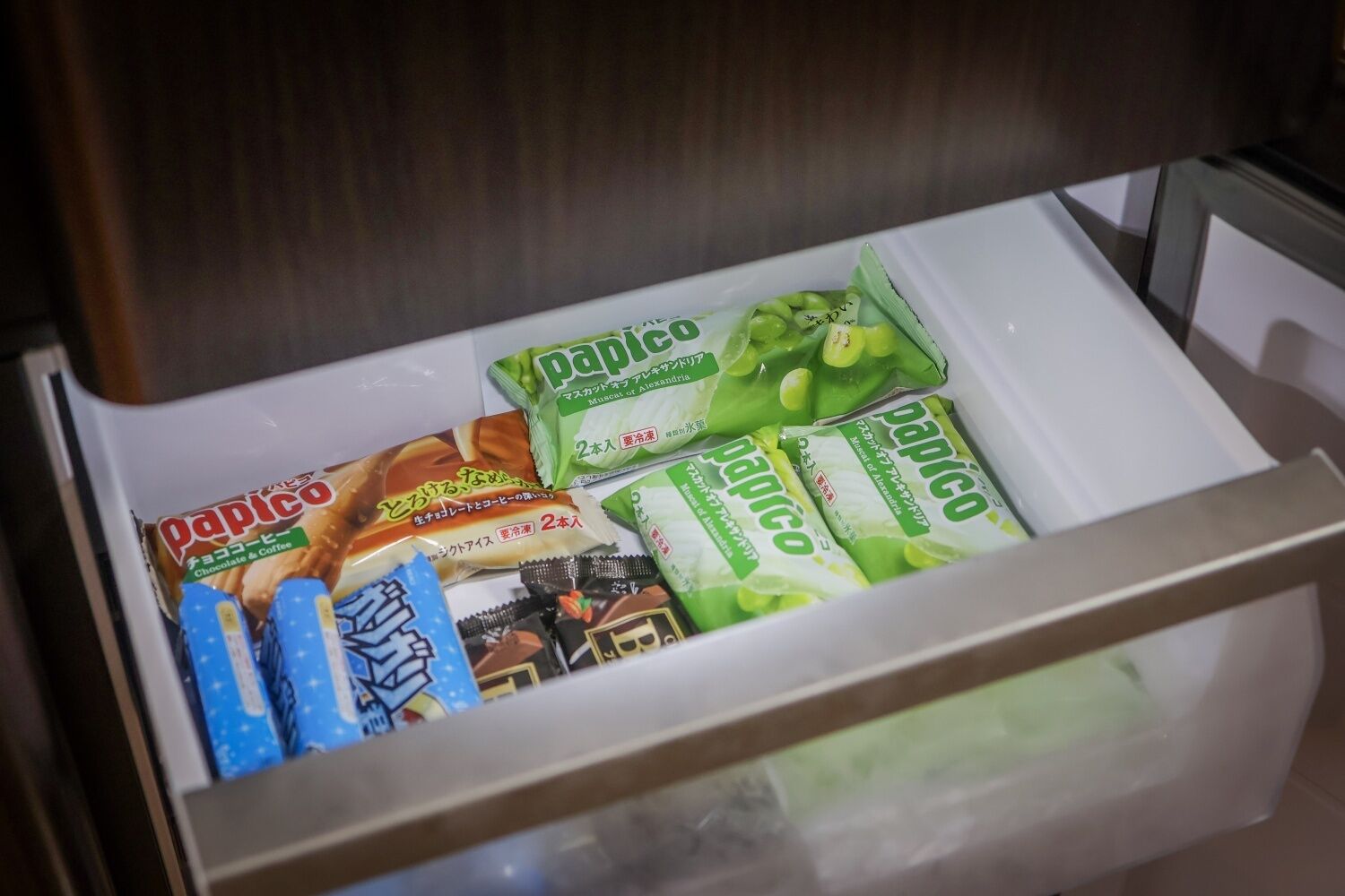 A drawer containing various packaged snacks including chocolate and coffee-flavored items, and green-flavored snacks.