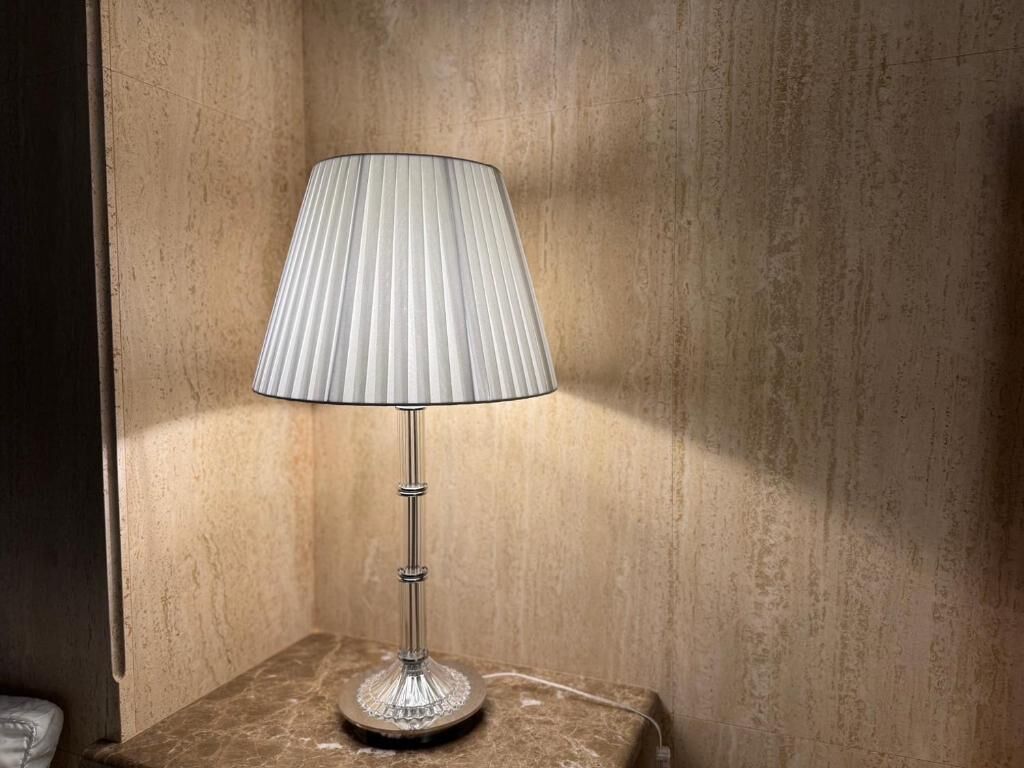 A table lamp with a ribbed lampshade on a marble table in a room with textured walls.