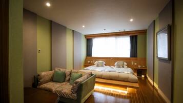A hotel room with a bed, a sofa, a small table, and a window with curtains.