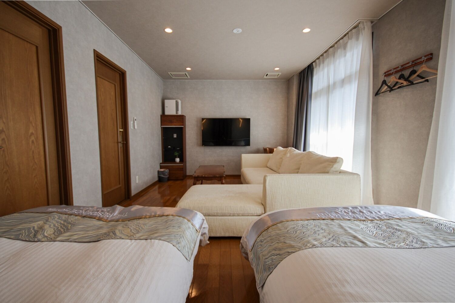 A hotel room with two beds, a sofa, a TV, and a window with curtains.