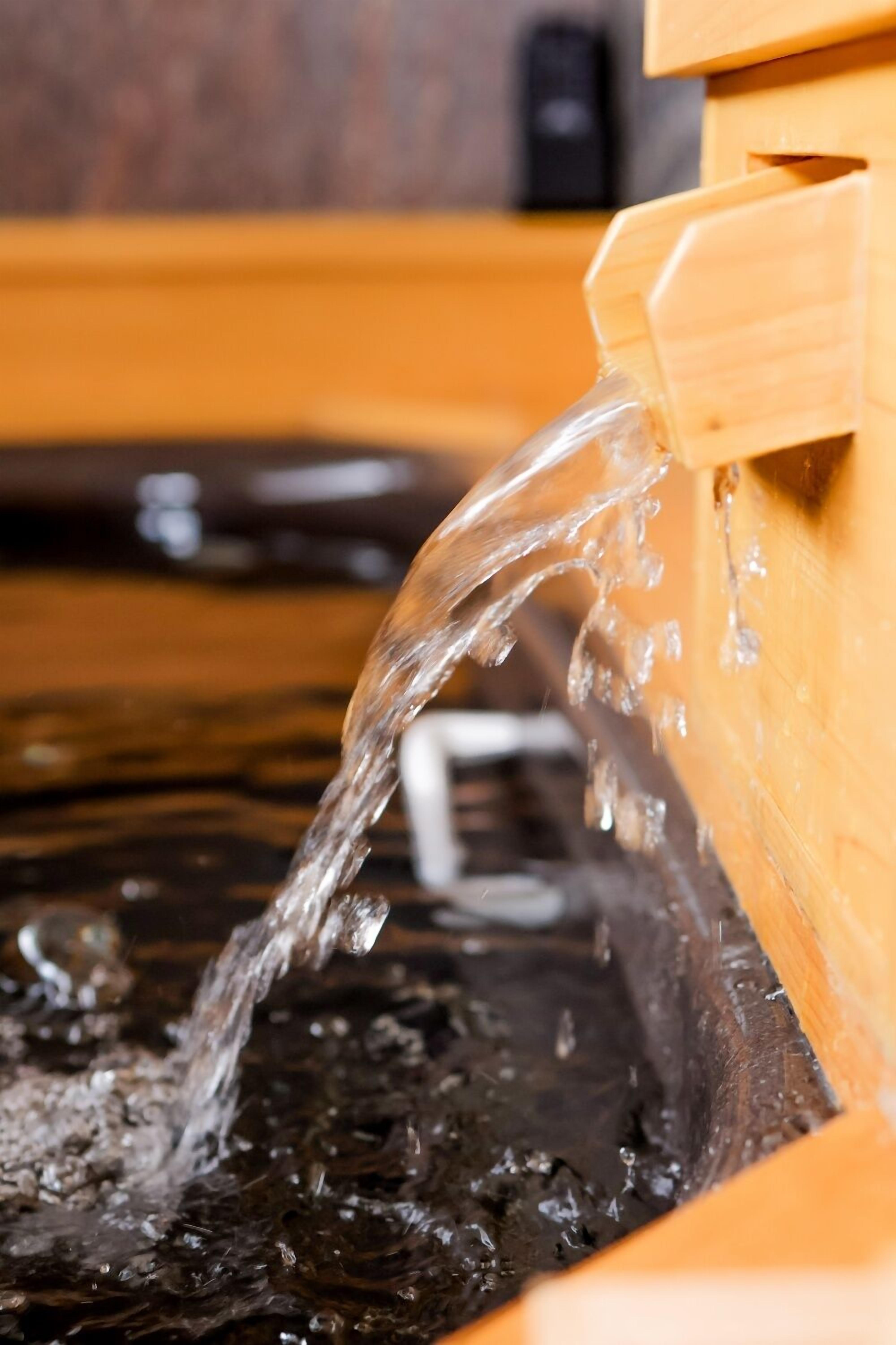 Una estructura de madera con agua brotando hacia un estanque oscuro y reflectante.