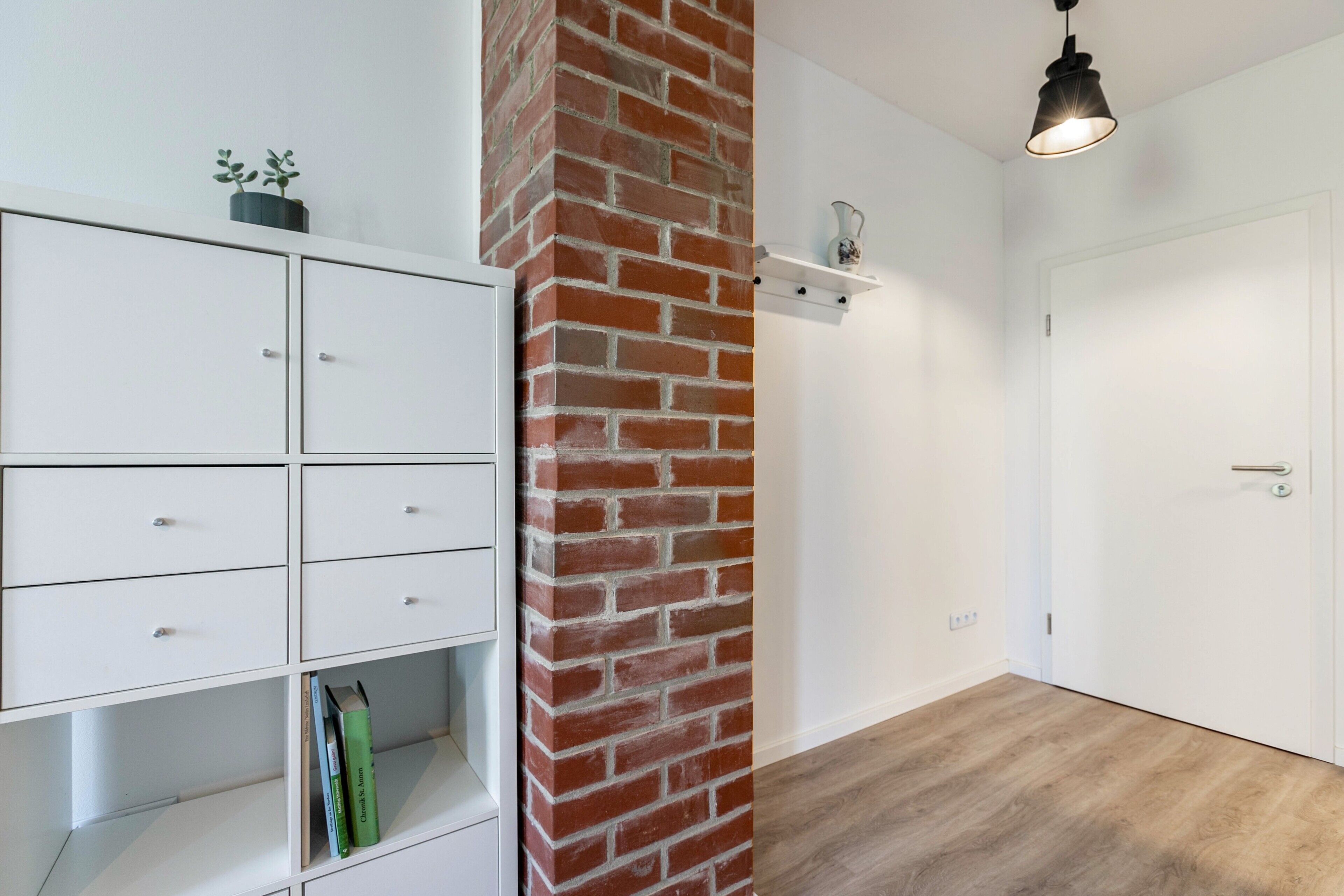 Ein Zimmer mit einem weißen Schrank, einer Ziegelwand, einem Holzboden, einer weißen Tür und einer hängenden Leuchte.