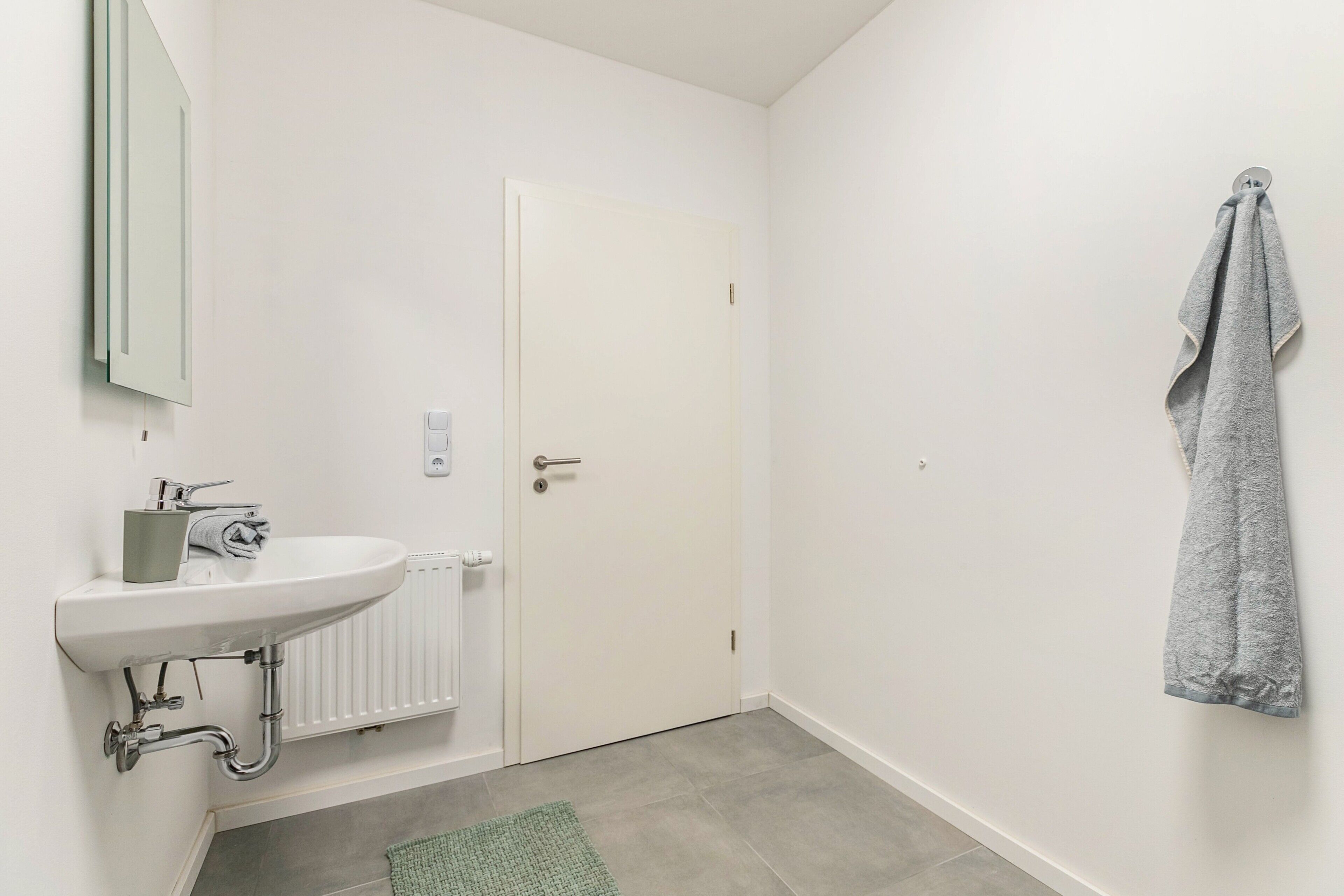 A bathroom with a white sink, a mirror, a towel hanging on the wall, and a closed door.