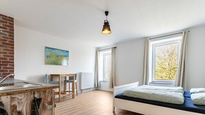 A compact room with a bed, a small table, a chair, a window with a view, and a hanging light fixture. - Holiday Apartment 'Hühnerhort' with Shared Terrace, Garden and Wi-Fi (Sankt Annen)