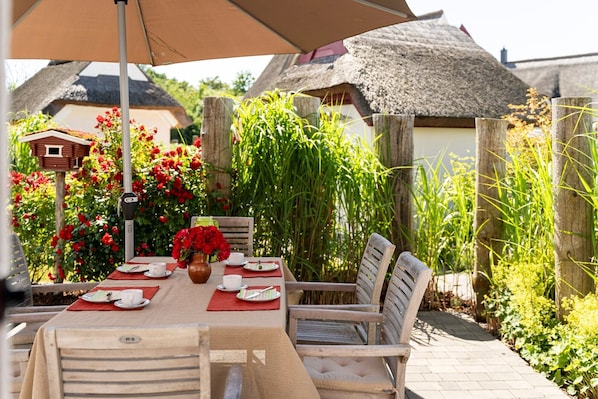 An outdoor dining area with a table set for two, surrounded by chairs and a large umbrella.