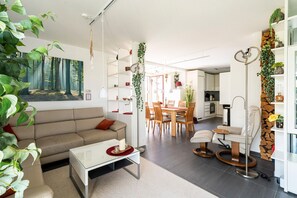 A modern living room with a sofa, coffee table, dining area with chairs, and a kitchen in the background.