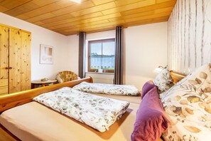 A room with two beds, a wooden wardrobe, a window with a view, and a small table with a bowl of fruit. - Apartment '55qm' with Private Terrace, Private Garden and Wi-Fi (Herscheid)