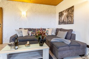 Un salon comprenant un canapé, une table basse, un vase avec des fleurs, une bouteille de vin et un luminaire fixé au mur.