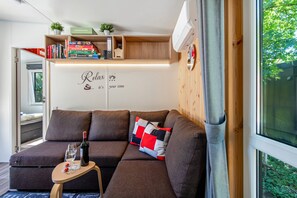 Un salon moderne avec un canapé, une petite table sur laquelle se trouvent une bouteille et des verres, et une bibliothèque remplie de livres et d’objets décoratifs.