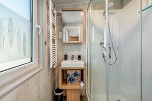 A bathroom with a glass shower enclosure, a sink with a mirror above it, and a window with a view of the sky.