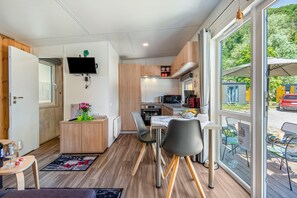 A compact kitchen with a dining area, a TV mounted on the wall, and a view of the outdoors.