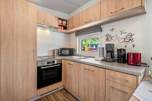 Une cuisine compacte dotée de meubles en bois, d’un four à micro-ondes, d’un grille-pain et d’une machine à café.