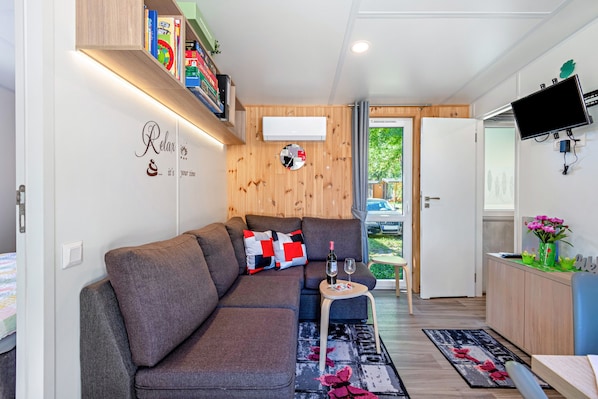 Ein modernes Wohnzimmer mit einer Couch, einem kleinen Tisch mit Flasche und Glas, einem Wand-Fernseher und einem Bücherregal.