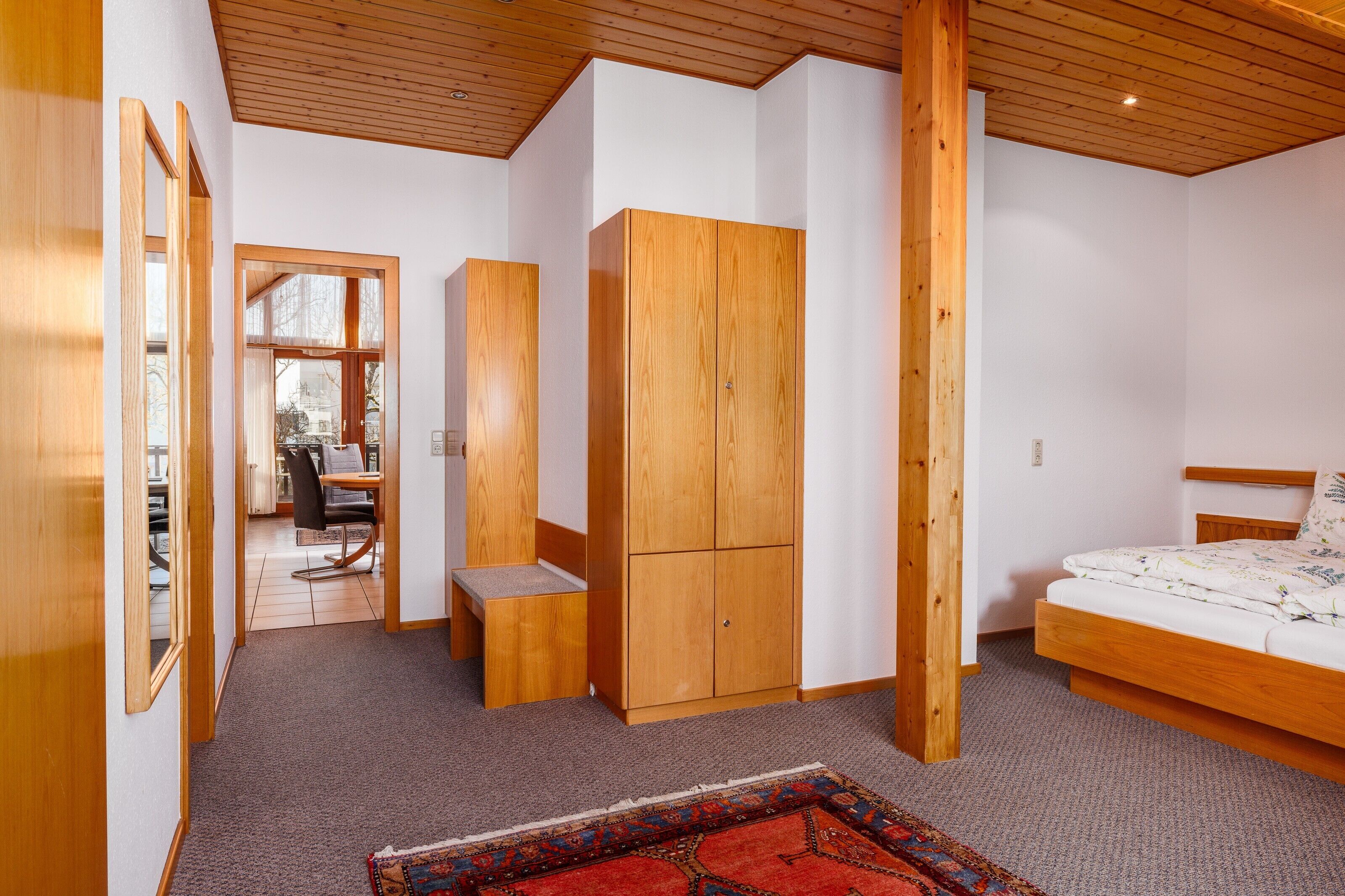 A bedroom with a wooden bed, a wardrobe, a desk with a chair, and a carpeted floor.