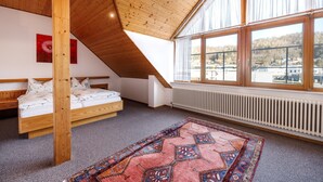 A bedroom with a sloped ceiling, a large window, a bed, a radiator, and a patterned rug.