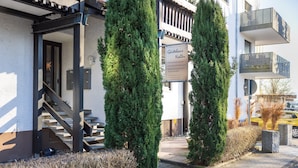 A building with a sign reading 'Gärtner Noller,' a staircase, and two tall evergreen trees.