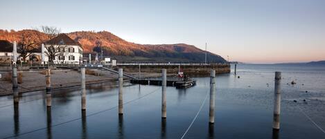 A calm waterfront with a dock, a bridge, and a building with a hill in the background.
