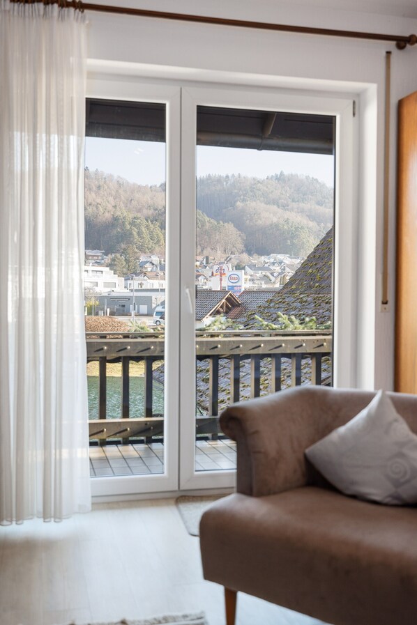 A room with a sliding glass door leading to a balcony with a view of a town and hills.