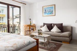 Ett modernt rum med en säng, en soffa, ett soffbord i glas och en tavla på väggen.