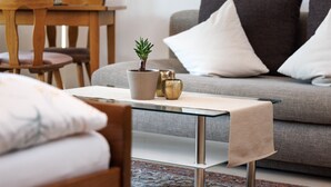 Una sala de estar con una mesa de centro de vidrio, un sofá gris y una pequeña planta en maceta.