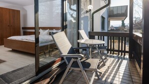 Un balcón con una cama, dos sillas, una mesita y un ventanal de vidrio que da a una habitación.