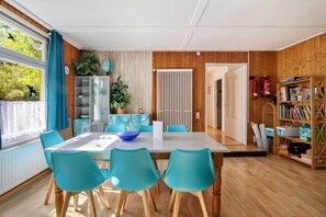 Un comedor con una mesa, sillas y un tazón azul. Se observa una estantería con libros y un globo terráqueo. También se ven un radiador y un extintor.
