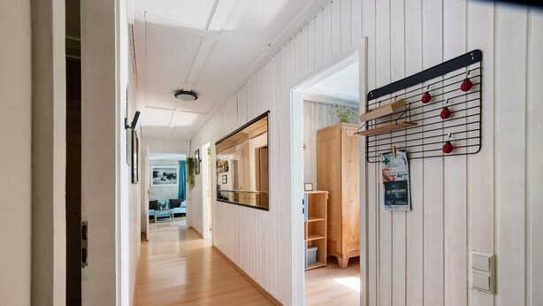 Un couloir doté d’un plancher en bois, un coin cuisine avec un meuble en bois, et une étagère murale sur laquelle sont disposés des objets rouges.
