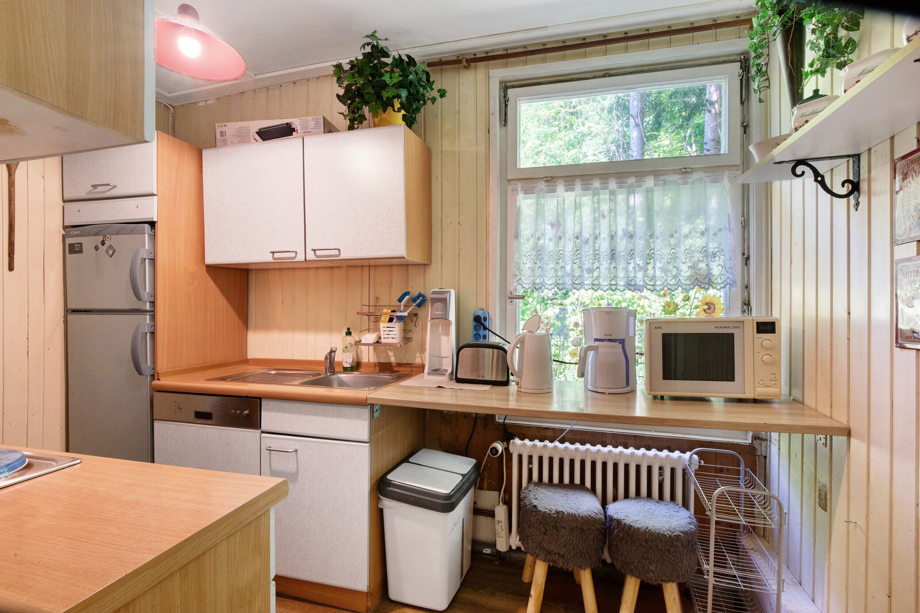 Una cocina compacta con refrigerador, microondas, pileta y un taburete pequeño.