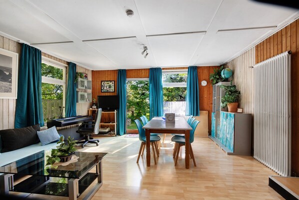 Una sala de estar moderna con comedor, suelo de madera y ventanas grandes con cortinas.