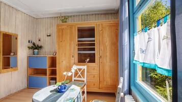 Ein Zimmer mit einem Holzschrank, einem Tisch mit blumigem Tuch, einem Stuhl und einem Fenster mit Vorhängen.