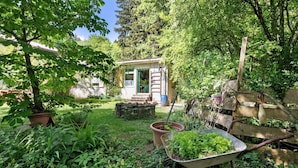 Un jardin rustique avec une petite maison en bois, une brouette et diverses plantes.