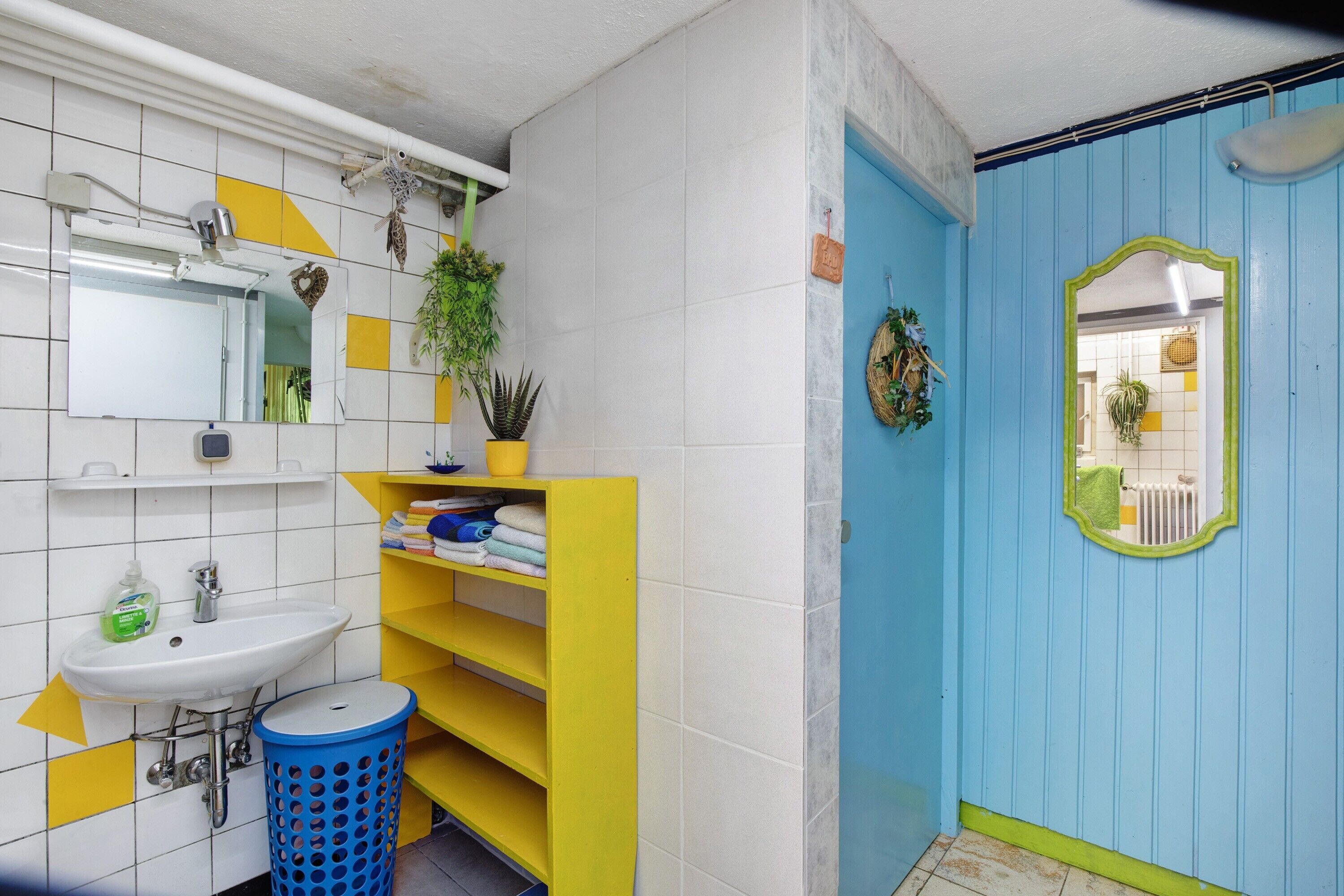 A bathroom with a sink, mirror, shelves, and a blue door.