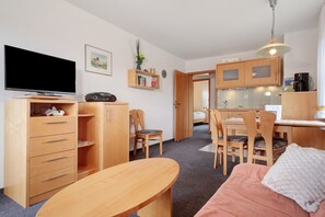 Ein kompakter Wohnraum mit Fernseher, Holzmöbeln, einer Küchenzeile und einem Essbereich.
