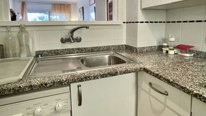 Een keuken met een roestvrijstalen spoelbak, een granieten aanrechtblad, witte kastjes en een ingebouwde vaatwasser.