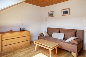 Une pièce comprenant une commode en bois, un canapé marron, une table basse en bois et deux tableaux encadrés accrochés au mur.