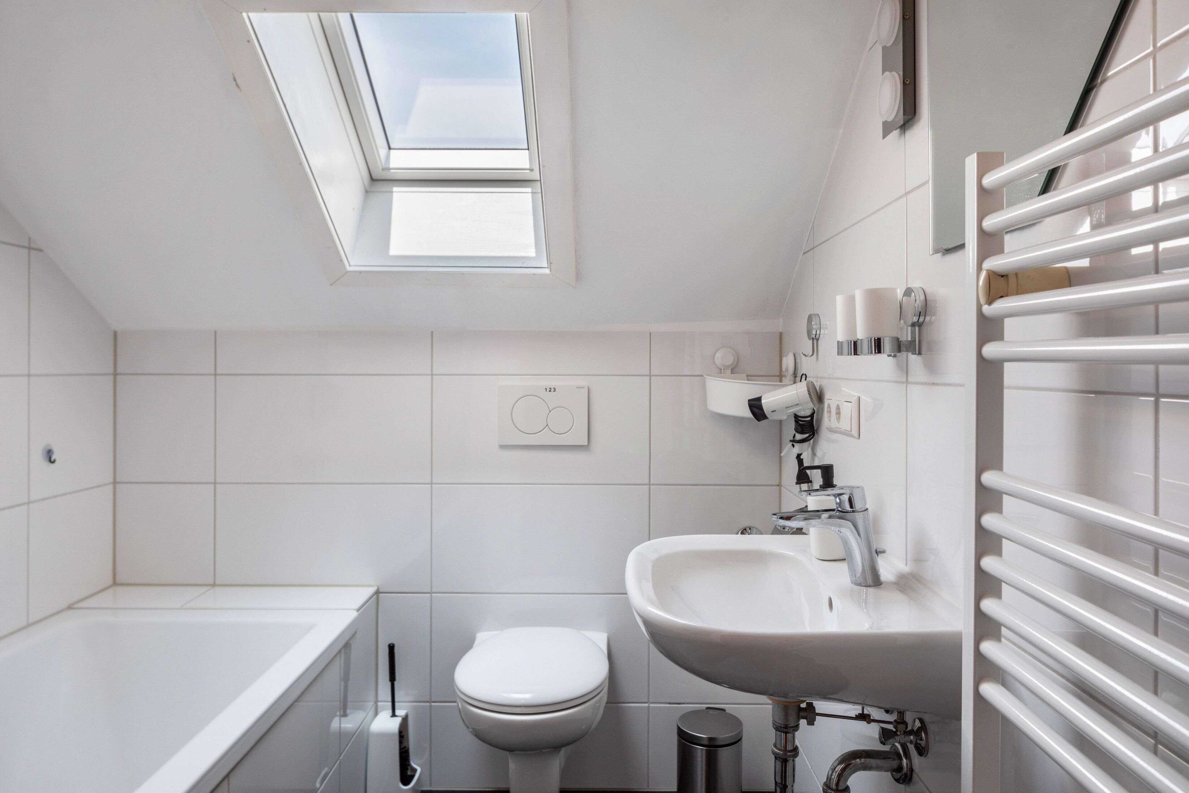 A modern bathroom with a skylight, a bathtub, a toilet, and a sink.