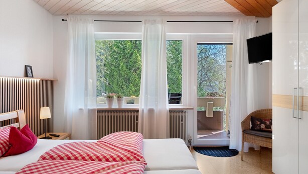 A hotel room with a bed, a television, a window with curtains, a radiator, and a chair.